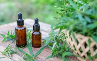 a setting of 2 bottles of CBD oil with a basket of marijuana leaves on a table