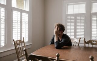A person struggling with aches and other health conditions sits at a table.